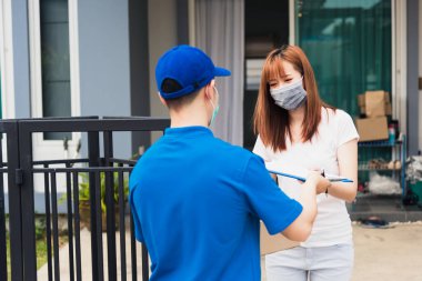 Paket postası taşıyan Asyalı genç teslimatçı, sokağa çıkma yasağı altındaki karantina altındaki kağıt defter üzerindeki kalem imzasını kullanarak koruyucu yüz maskeli kadın müşteri COVID-19 'u karantina altına aldı.