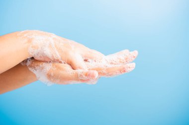 Kapalı vücut bakımı Asyalı genç kadın ellerini sabunla yıkıyor köpük, hijyen önleme COVID-19 veya koronavirüs koruma konsepti var, mavi arka planda izole edilmiş.