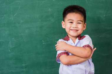 Okula geri dön. Anaokulundaki çocuk üniformalı mutlu Asyalı komik çocuk yeşil okul tahtasına gülümsüyor ve ilk kez okul eğitimi kavramına atölye çekimine katılıyor.