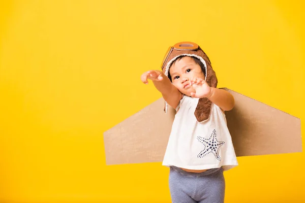 幸せなアジアの美しい面白い赤ちゃんの女の子の笑顔は おもちゃの段ボール飛行機の翼が飛ぶと手を再生し ゴーグルを上げるパイロットの帽子を身に着けている スタジオショット孤立黄色の背景 スタートアップの自由コンセプト — ストック写真
