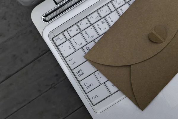 Ahşap gri arka plan üzerinde beyaz dizüstü bilgisayarda kahverengi zarf bırakır.