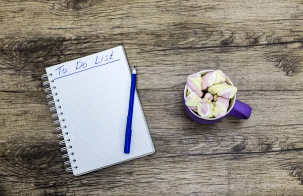 Xícara de marshmallows com notebook sobre fundo de madeira . — Fotografia de Stock