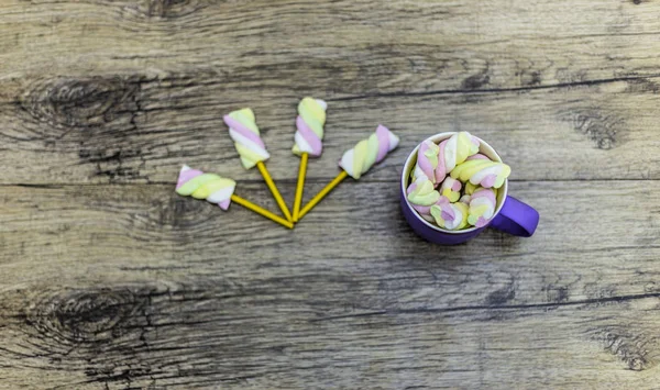 cup of marshmallows with sticks on wooden background.