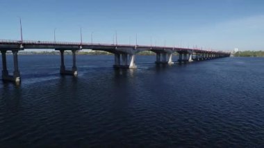 Şehir nehrinin üzerinden naklediliyor. Arabalar her iki yönde de köprüde hareket ediyor. Nehir üzerinde karayolu köprüsünde giden araba panoramik üstten görünüşü gökyüzü yüksekliği, helikopter dronu.