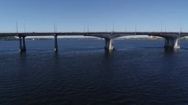 Şehir nehrinin üzerinden naklediliyor. Arabalar her iki yönde de köprüde hareket ediyor. Nehir üzerinde karayolu köprüsünde giden araba panoramik üstten görünüşü gökyüzü yüksekliği, helikopter dronu.