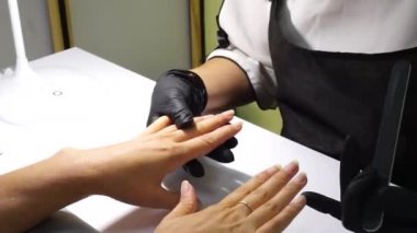 manicure In the beauty salon they do manicure for the girl. Manicurist in pink gloves and a nail file in hands. Nail files. Top view. Close-up. Slow motion.