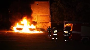 A car is burning and gasoline is dripping and burning. Unrecognizable firefighter spraying water and foam for extinguishing the fire. Loopable seamless animation cinemagraph