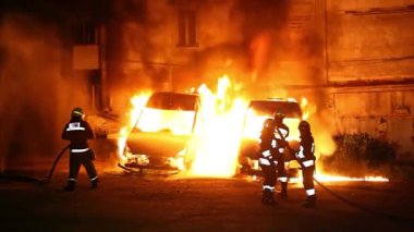 A car is burning and gasoline is dripping and burning. Unrecognizable firefighter spraying water and foam for extinguishing the fire. Loopable seamless animation cinemagraph