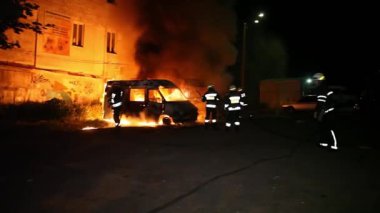 A car is burning and gasoline is dripping and burning. Unrecognizable firefighter spraying water and foam for extinguishing the fire. Loopable seamless animation cinemagraph