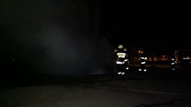 A car is burning and gasoline is dripping and burning. Unrecognizable firefighter spraying water and foam for extinguishing the fire. Loopable seamless animation cinemagraph