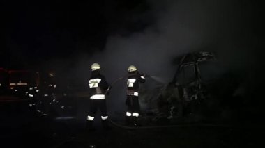 A car is burning and gasoline is dripping and burning. Unrecognizable firefighter spraying water and foam for extinguishing the fire. Loopable seamless animation cinemagraph