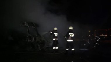 A car is burning and gasoline is dripping and burning. Unrecognizable firefighter spraying water and foam for extinguishing the fire. Loopable seamless animation cinemagraph