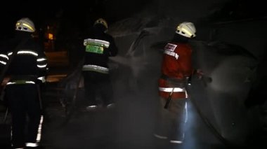 A car is burning and gasoline is dripping and burning. Unrecognizable firefighter spraying water and foam for extinguishing the fire. Loopable seamless animation cinemagraph