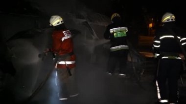 A car is burning and gasoline is dripping and burning. Unrecognizable firefighter spraying water and foam for extinguishing the fire. Loopable seamless animation cinemagraph