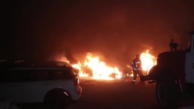 Şehir caddesinde yangın söndürücüyle yangını söndürmeye çalışan ama içerisi tamamen yanmış bir araba yangını.