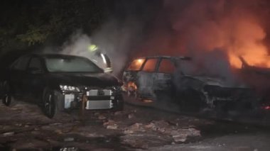 Şehir caddesinde yangın söndürücüyle yangını söndürmeye çalışan ama içerisi tamamen yanmış bir araba yangını.