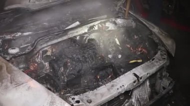 Şehir caddesinde yangın söndürücüyle yangını söndürmeye çalışan ama içerisi tamamen yanmış bir araba yangını.