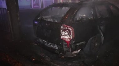 Şehir caddesinde yangın söndürücüyle yangını söndürmeye çalışan ama içerisi tamamen yanmış bir araba yangını.