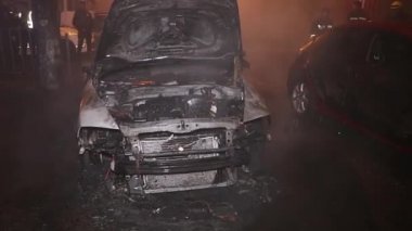 Şehir caddesinde yangın söndürücüyle yangını söndürmeye çalışan ama içerisi tamamen yanmış bir araba yangını.