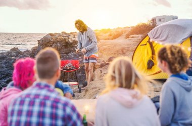 Mutlu arkadaş sahilde çadır kamp grup ve eğlenceli bir yapım barbekü barbekü akşam yemeği - genç insanların hazırlama ve okyanus - tatil, gençlik yanında bira içme, yaşam kavramı seyahat
