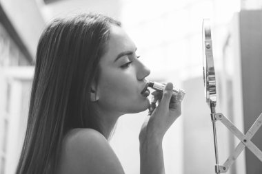 Beautiful young woman putting her lipstick on before going out for a night in town - Stunning girl applying makeup on and getting ready to go out in the club - Black and white vintage editing clipart