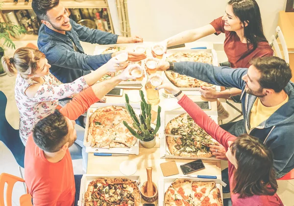 Group of friends toasting glasses of beer while eating pizza in their house - Happy people enjoying dinner together with tasty take away food at home - Concept of friendship, company, lifestyle