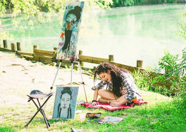 Young artist girl drawing draft of next painting on park near lake - Painter woman with dreadlocks hairstyle working on her art in the city outdoor - Concept of people expressing arts