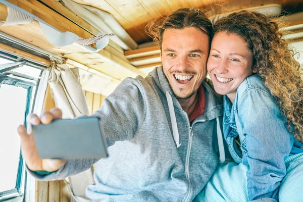 Happy man and woman taking a selfie with a mobile smart phone camera - Travel couple making pictures of their journey on a vintage minivan with wood interior - Travel, love, technology concept — Stock Photo, Image