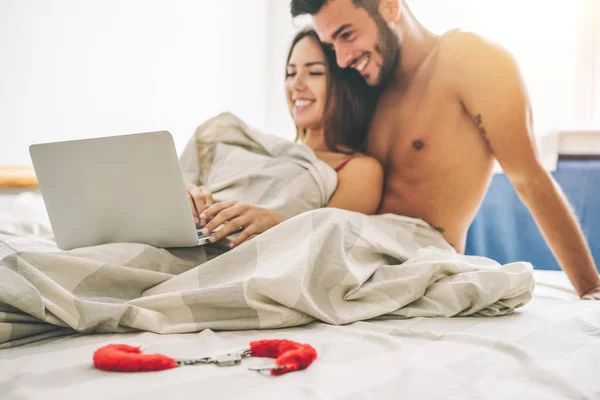 幸福的年轻夫妇躺在床上与计算机美丽的已婚夫妇看角色游戏的性爱视频笔记本电脑笑在一起 技术概念 软的重点放在床单上 — 图库照片