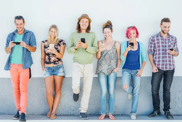 Young people watching on their smart mobile phones leaning on a wall - Generation addicted to new technology - Concept of youth addiction to social network trends