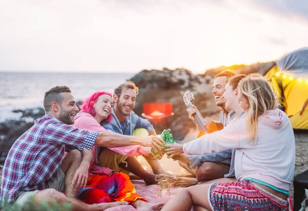 Group of friends cheering with beers outdoor - Happy people camping with tent and making a barbecue having fun toasting bottles of beer - Friendship, lifestyle, camp concept