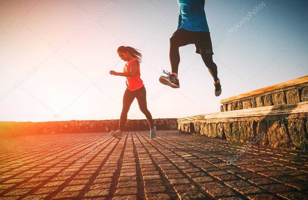 Health fit young couple running together during a magnificent sunset - Athletic friends doing sport outdoor - Sporty people training with jump exercises - Relationship, sport, lifestyle concept