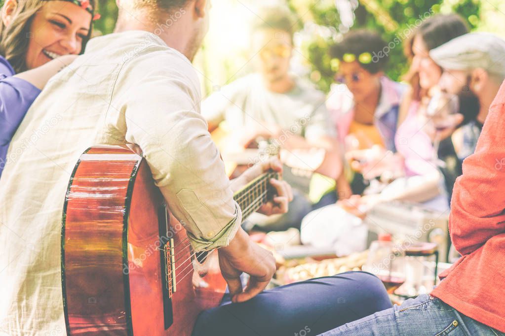 Group of friends having a picnic in a park outdoor - Happy young mates enjoying pic-nic playing guitar, singing and drinking wine eating food - Recreation concept - Focus on man arm's with guitar
