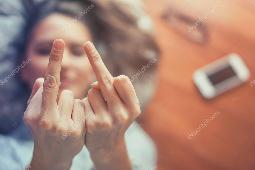Woman's hand gesturing with middle fingers while lying on the floor of her apartment - Close up of young girl flipping off in front of camera at home - Arrogant, people, youth concept