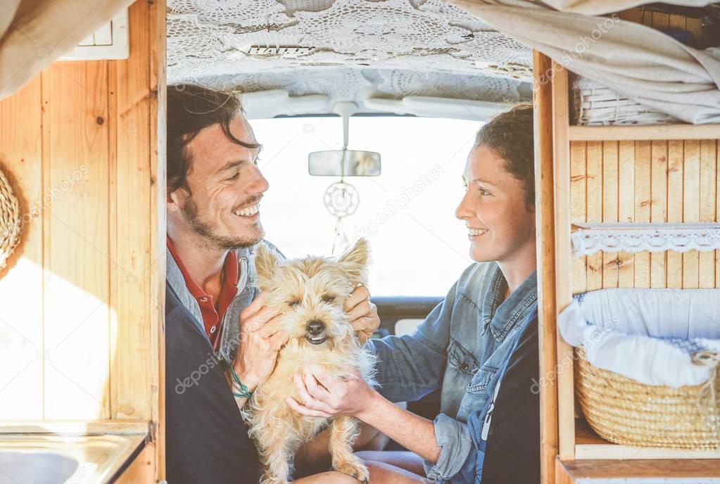 Happy couple cuddling their dog inside a mini van - Young people getting ready for a road trip having fun together with their pet - Love, travel, happiness concept