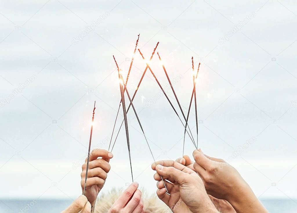 Close up hands of group of happy friends having fun celebrating with sparklers fireworks outdoor - Youth, celebrate, party lifestyle concept