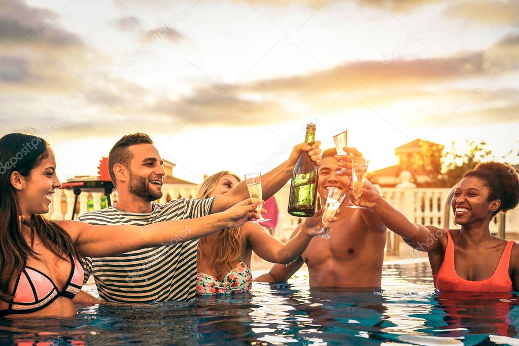 Group of happy friends making a pool party cheering with champagne at sunset - Young people laughing and having fun toasting with sparkling wine in luxury tropical resort - Youth lifestyle concept