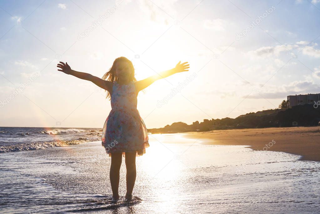 Happy child spreading her hands up on the beach on a magnificent sunset - Baby girl having fun in vacation holidays - Childhood, children, happiness concept