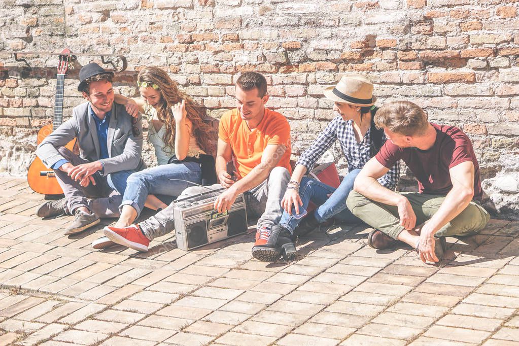 Group of friends enjoying together a sunny day outdoor listening music with a vintage stereo - Happy young people having fun sitting outside university - Concept of friendship, lifestyle and music