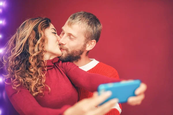 Casal feliz tirando selfie com câmera de smartphone móvel - Jovens amantes românticos beijando e celebrando férias de Natal - Relacionamento amoroso, xmas e conceito de tendências tecnológicas — Fotografia de Stock