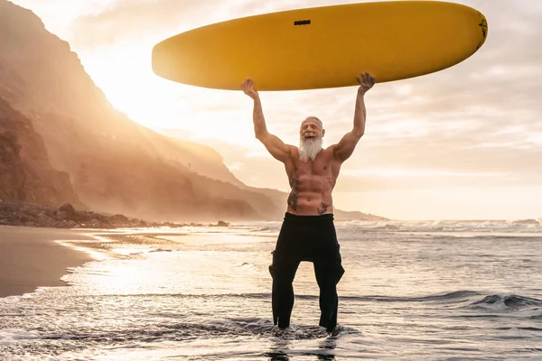 Happy fit senior, весело занимающийся серфингом на закате - тренировка мужчины с доской для серфинга на пляже - образ жизни пожилых здоровых людей и концепция экстремальных видов спорта — стоковое фото