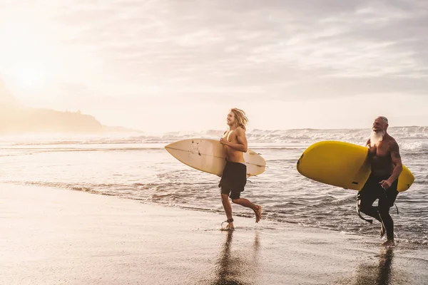 Happy fit friends having fun surfing on sunset time - Surfers father and son running out the ocean - Sporty people lifestyle and extreme sport concept — Stock Photo, Image