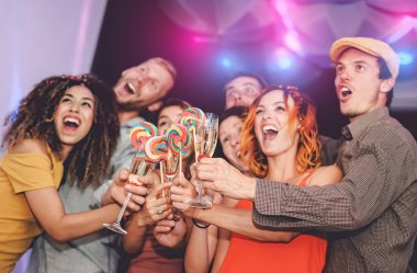 Mutlu arkadaşlar şampanyayla kadeh kaldırırken ve disko kulübünde lolipop yerken - grup gençleri yeni yıl partisini kutlarken - gençlik kültürü tatil yaşam tarzı konsepti