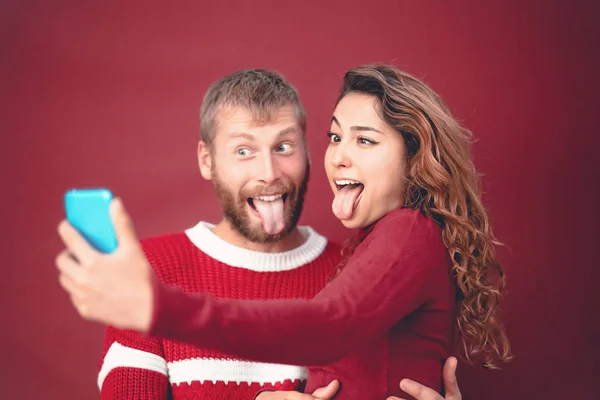 แฮปปี้บ้าคู่ถ่ายเซลฟี่ในขณะที่ทําหน้าโง่ ๆ กับกล้องสมาร์ทโฟนมือถือ - คนหนุ่มสาวเฉลิมฉลองวันหยุดคริสต์มาส - ความสัมพันธ์ความรัก, xmas และแนวโน้มเทคโนโลยี ภาพสต็อก