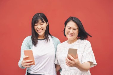 Asyalı anne ve kız açık havada cep telefonu kullanıyor mutlu Çinli aile yeni teknoloji eğilimli sosyal medya uygulamaları ile eğleniyor teknoloji bağımlılığı yaşam tarzı insanlar kavramı