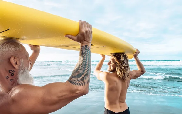 Happy fit friends having fun surfing on tropical ocean - Surfers father and son doing stretching surf exercises - Sporty people lifestyle and extreme sport concept — Stock Photo, Image