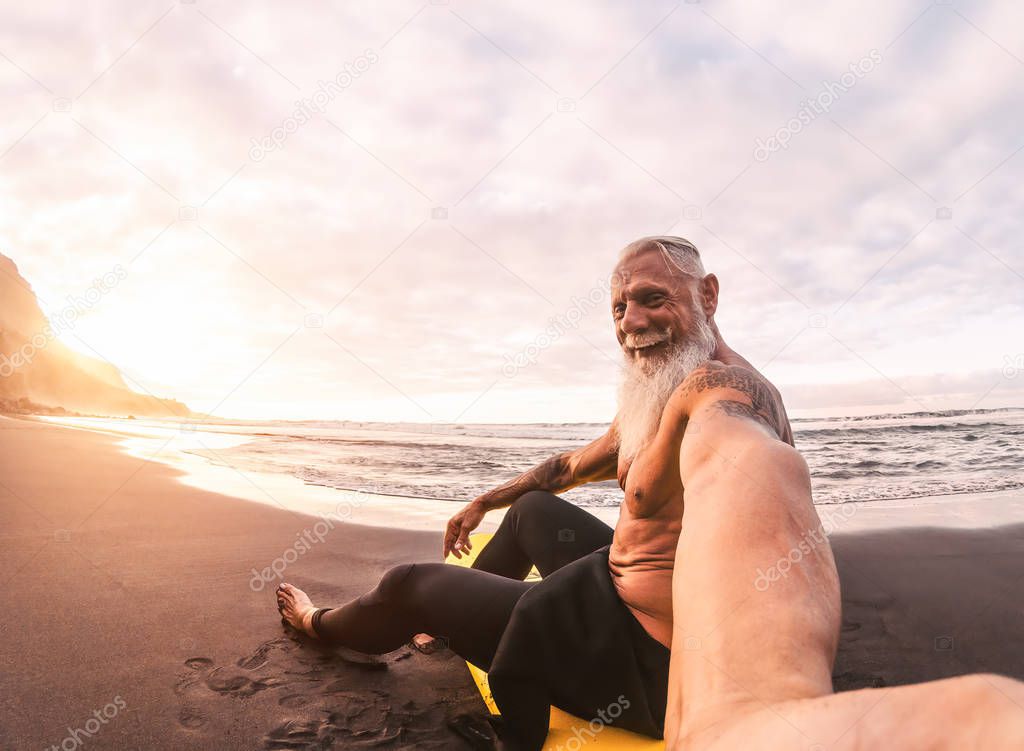 Senior man taking selfie in surfing day - Mature hipster male having fun doing surf at sunset time - Elderly health people lifestyle and extreme sport concept