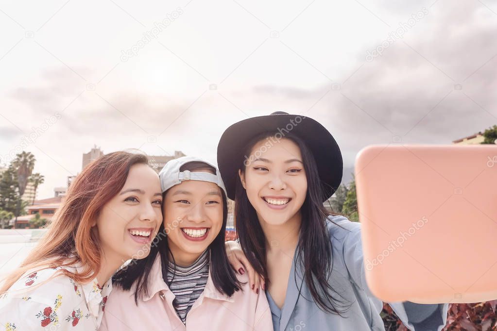 Happy Asian girls taking selfie with mobile smartphone outdoor - Young trendy social friends having fun using new technology apps - People, millennial generation and youth lifestyle concept