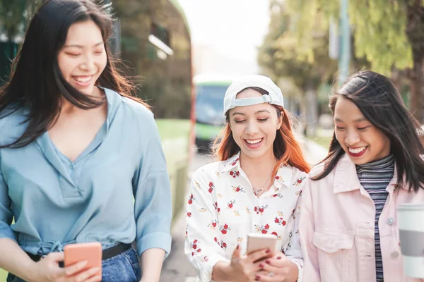Felices novias asiáticas caminando por la ciudad mientras ven en teléfonos inteligentes móviles - Jóvenes adolescentes divirtiéndose con nuevas aplicaciones de redes sociales - Generación milenaria juvenil y concepto de tecnología — Foto de Stock