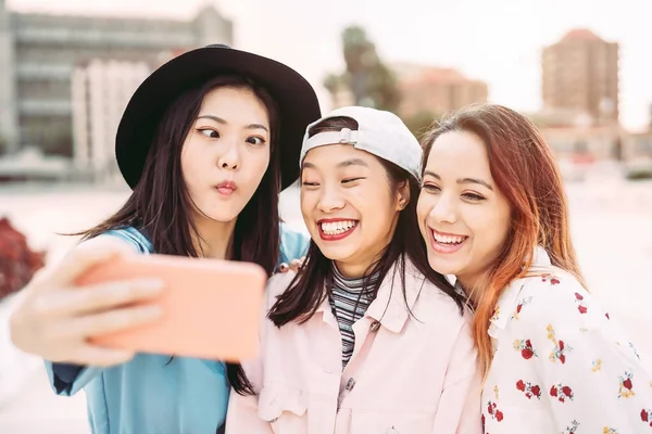 Chicas asiáticas felices tomando selfie con teléfono inteligente móvil al aire libre - Jóvenes amigos sociales juguetones divertirse utilizando la nueva tecnología de moda - Personas, generación milenaria y el concepto de estilo de vida juvenil — Foto de Stock